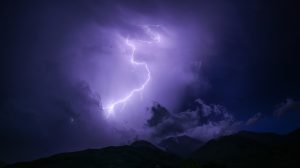 夜間雷暴中劃破紫色烏雲的巨大閃電，下方為黑暗的山脈輪廓。